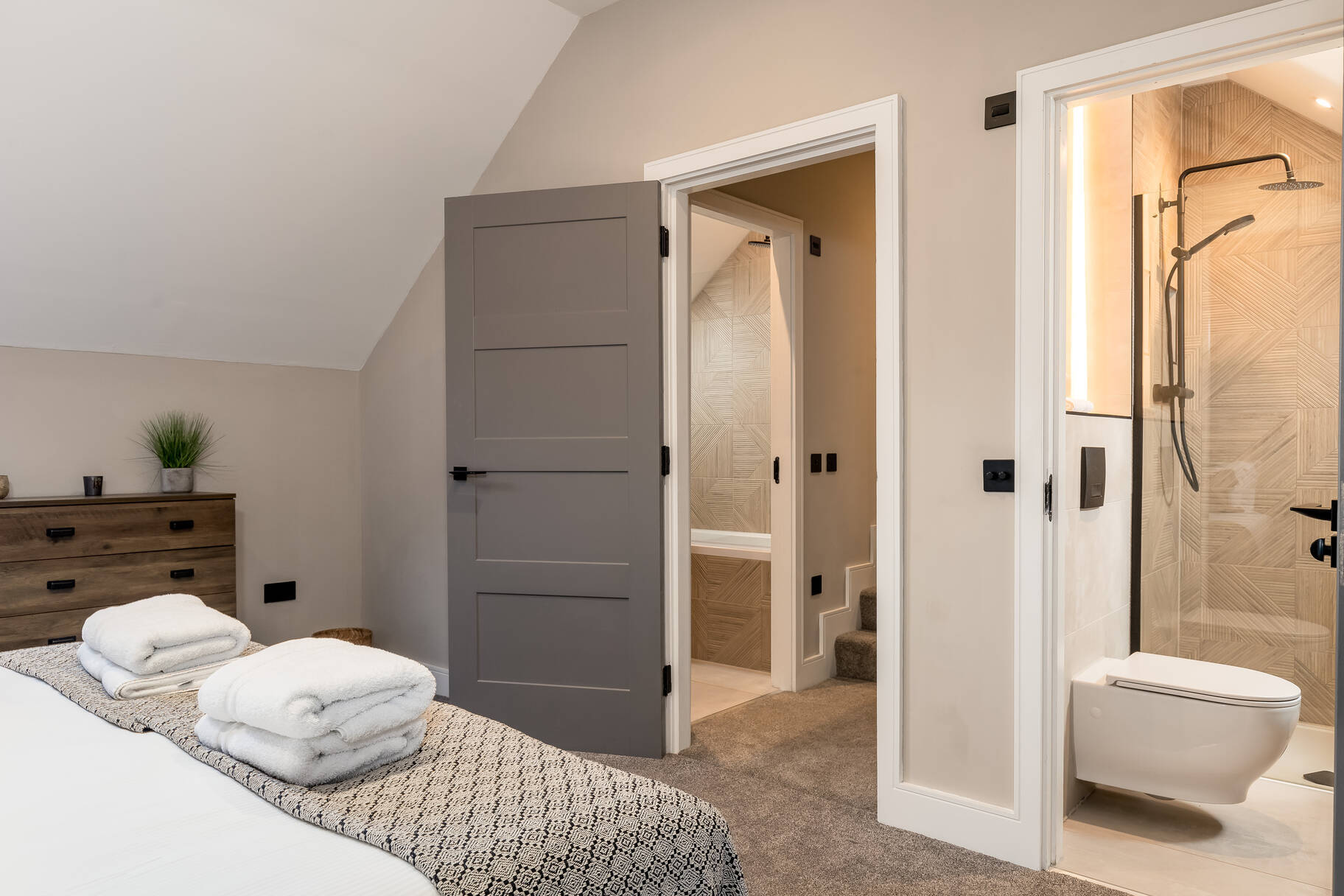 Bedroom corner showing the ensuite shower with chevron-tile wall and wooden chest of drawers