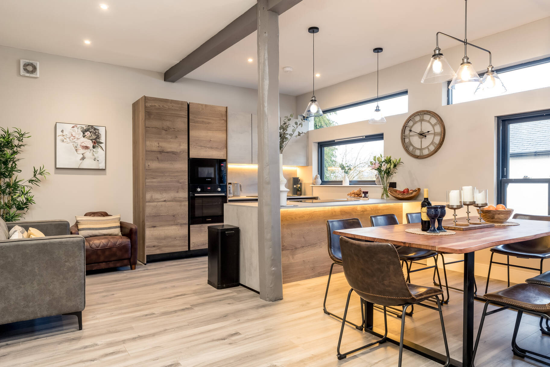 Open-plan kitchen-diner with oak table, brown leather chairs, glass pendants and big station clock