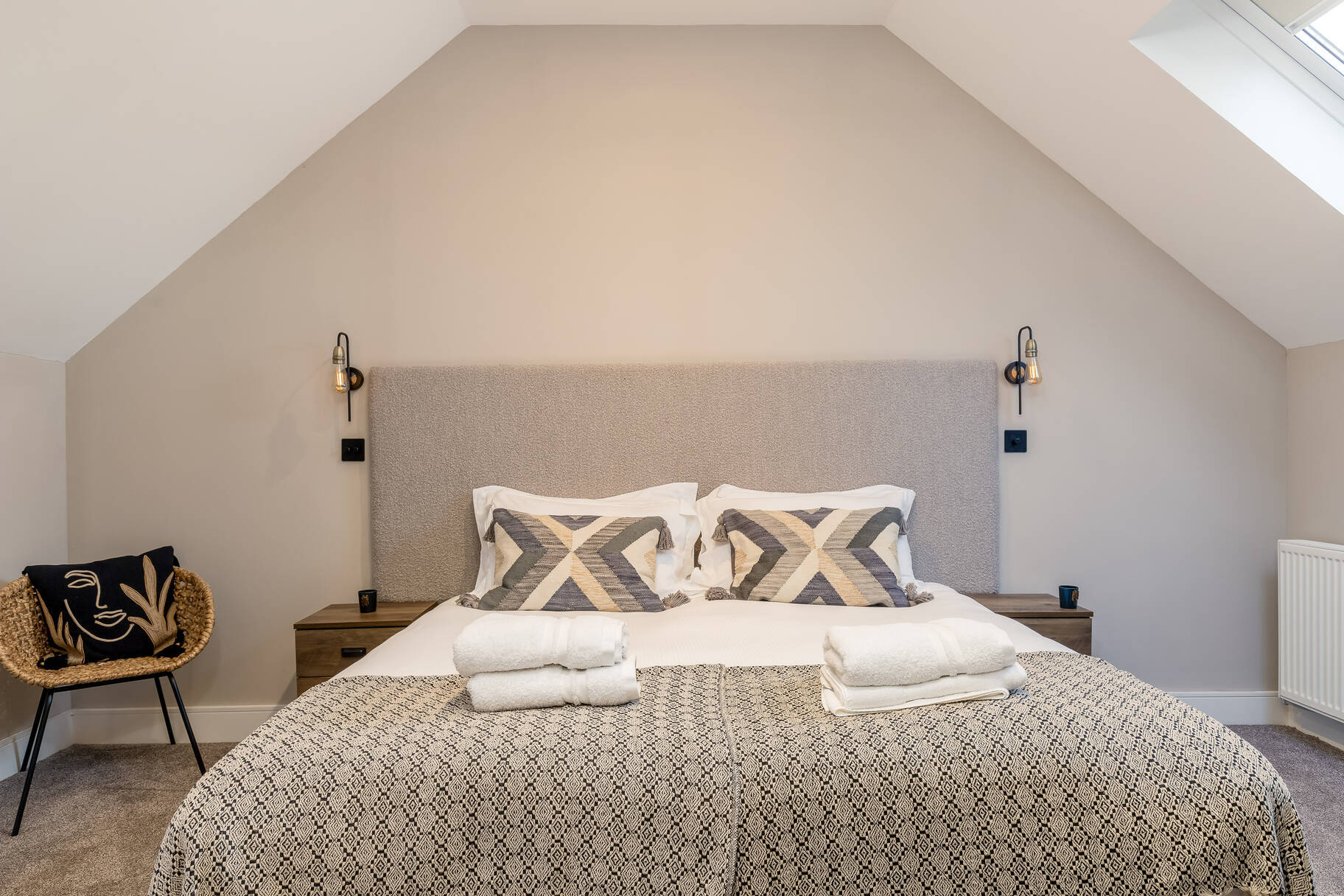 Vaulted master bedroom with king bed, grey boucle headboard and skylight under sloped ceiling