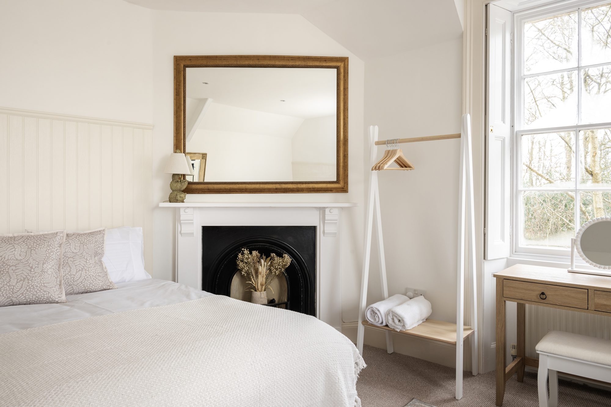 Cream attic bedroom with cast-iron fireplace, gold-framed mirror and open clothes rail