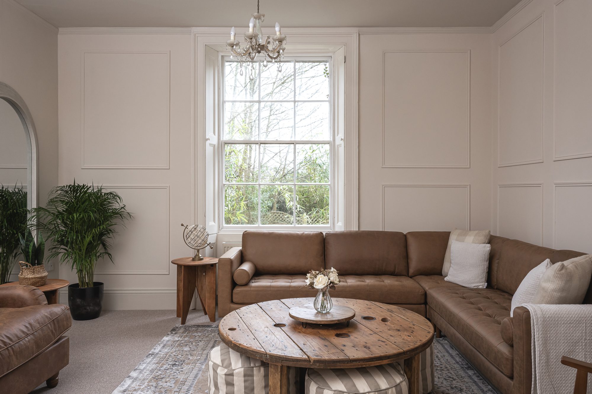 Panelled lounge with corner leather sofa, cable-reel coffee table and chandelier above sash window