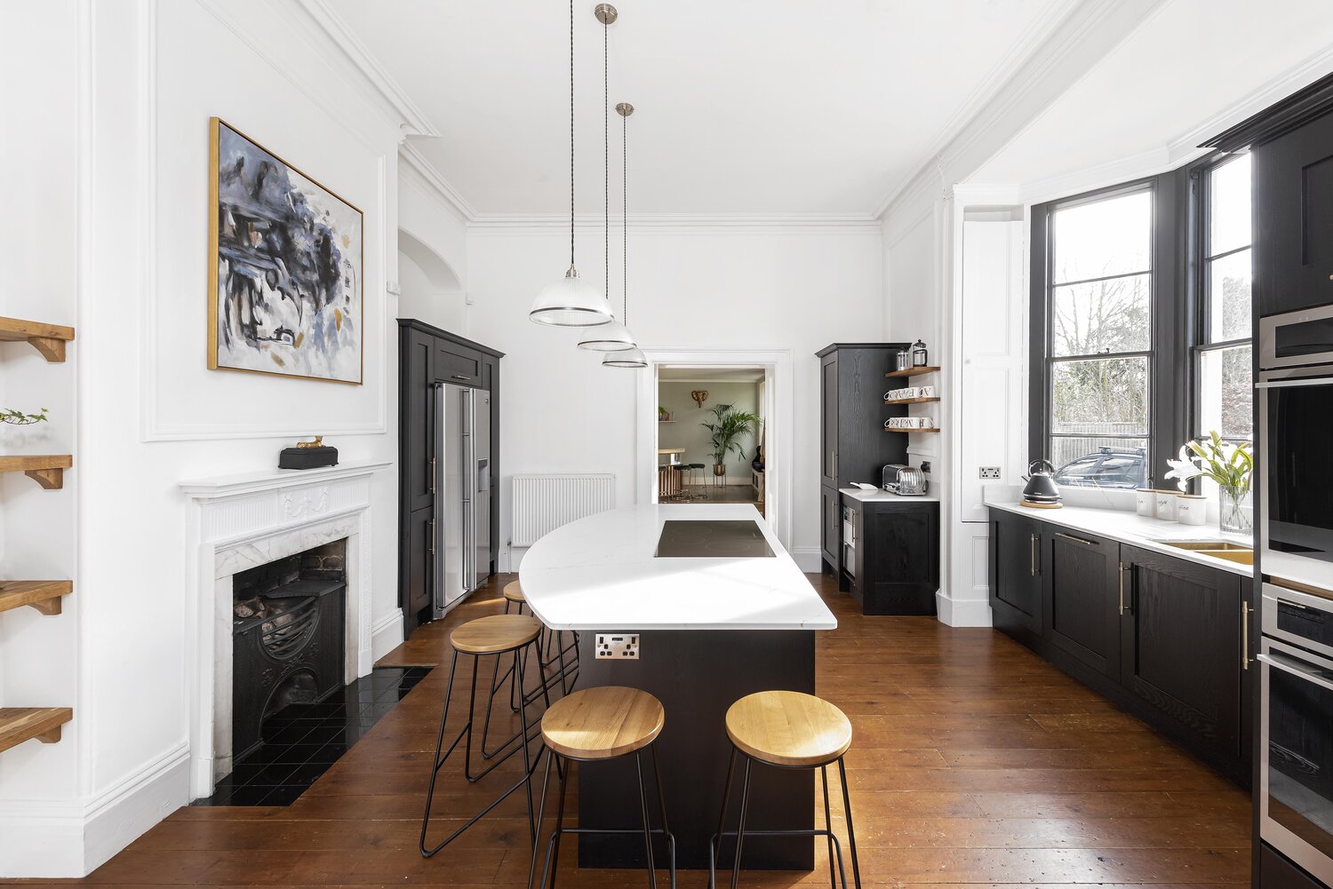 Black and white kitchen with marble-topped island, three wooden barstools, white pendant lights, abstract painting and a small marble fireplace.