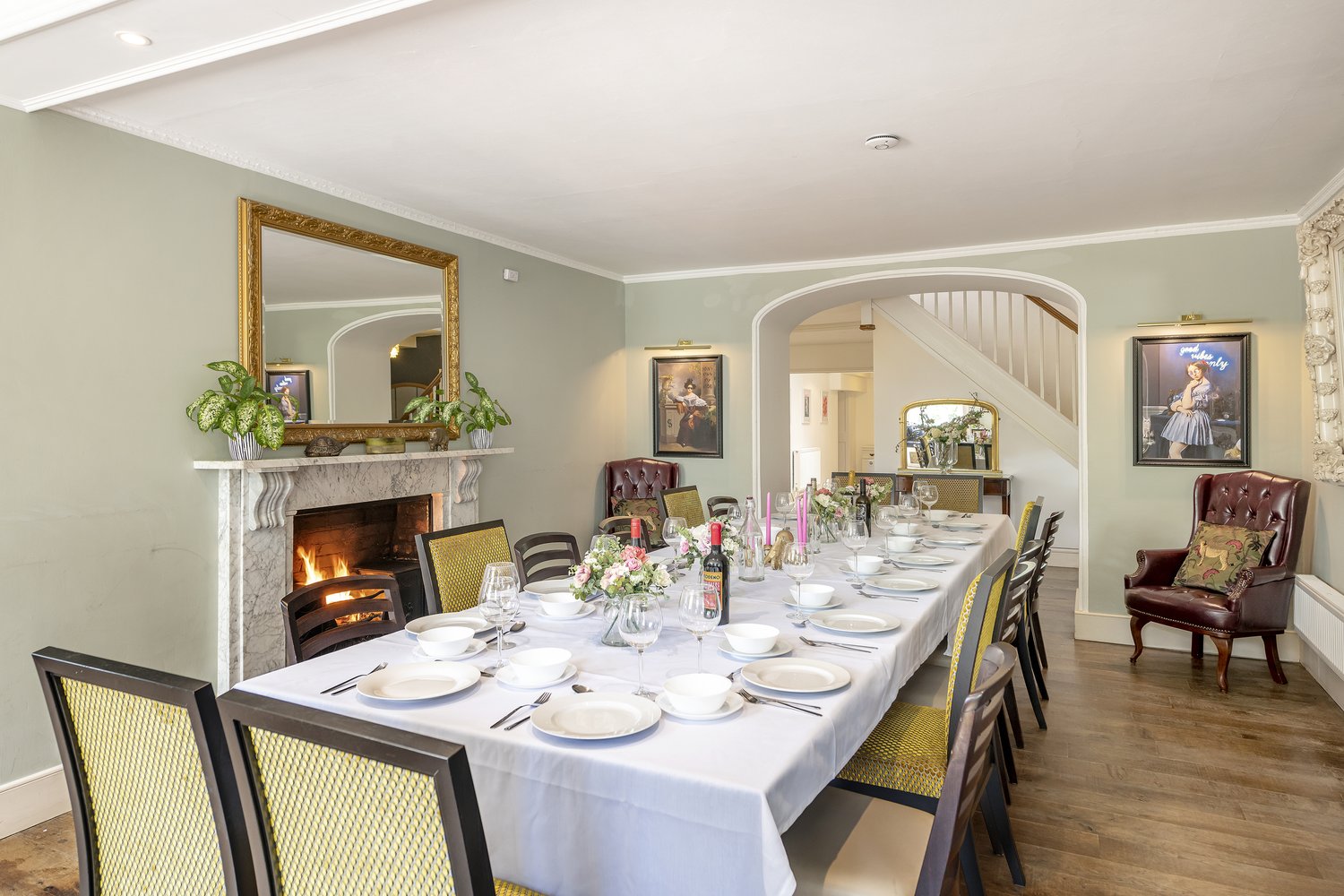 Wide kitchen view with a marble-topped island over a wine-bottle rack, two stools, black sash bay window and a sage room visible through an open doorway.