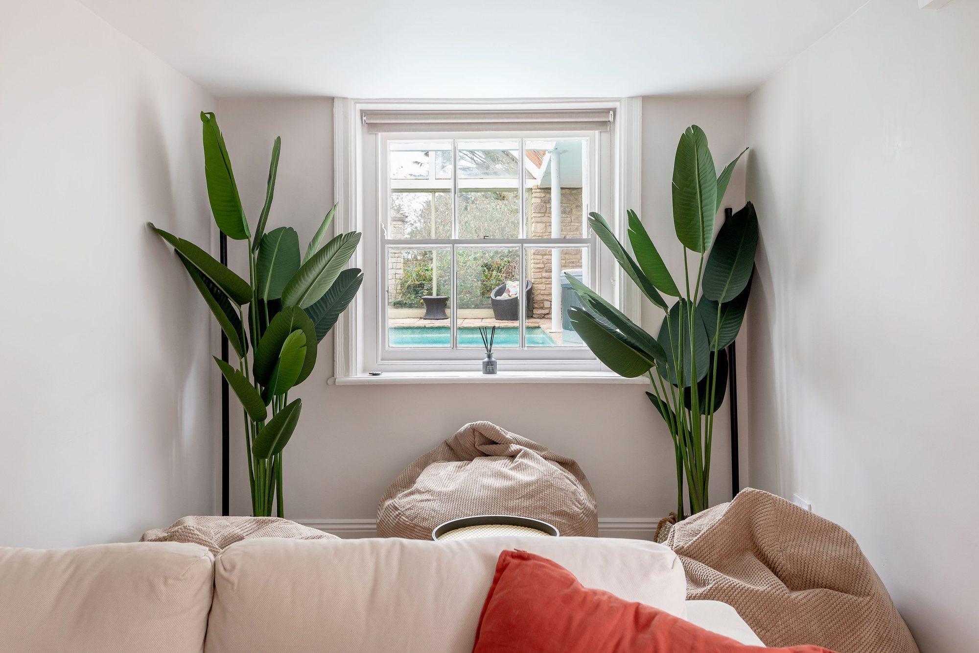Snug nook with two tall banana plants framing a sash window that looks out onto the pool terrace