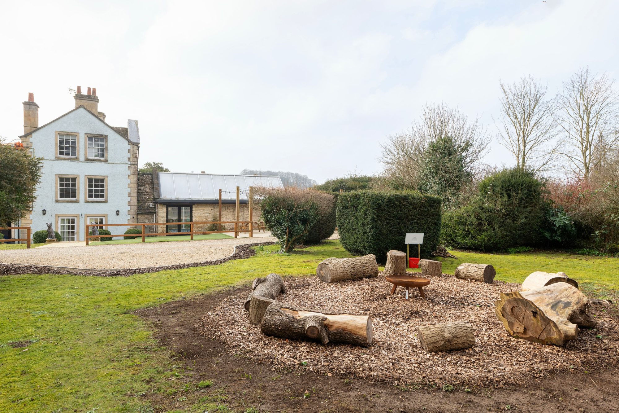 Cream country house front exterior at Beau's Spa House with gravel approach and a garden firepit ringed by log seats