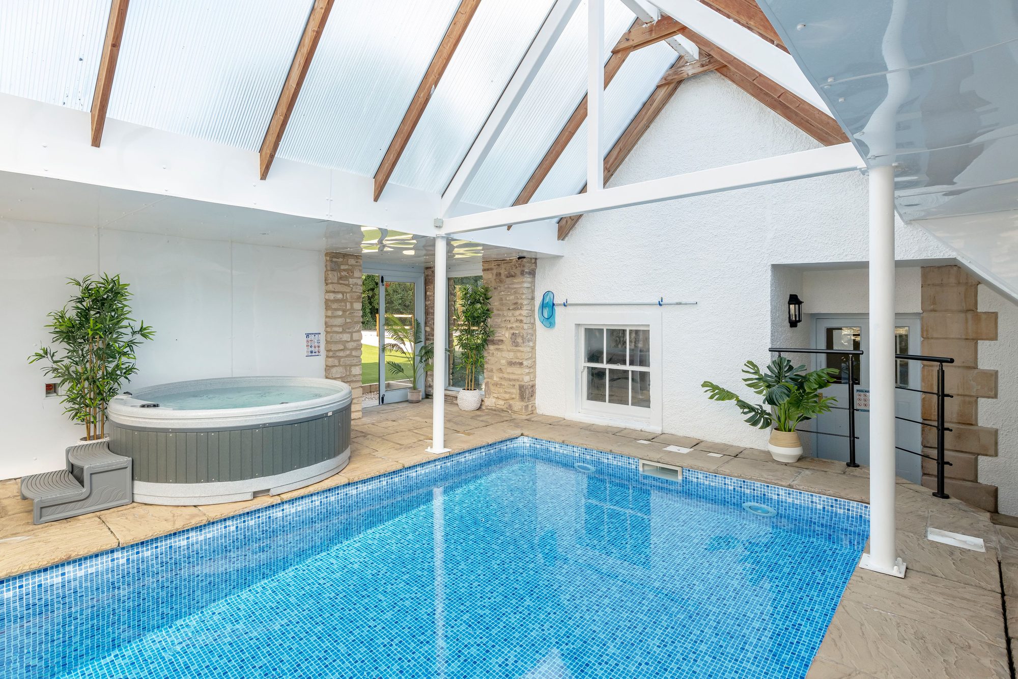 Beau's Spa House indoor pool from the hot tub end, vaulted roof, exposed stone wall and tropical plants