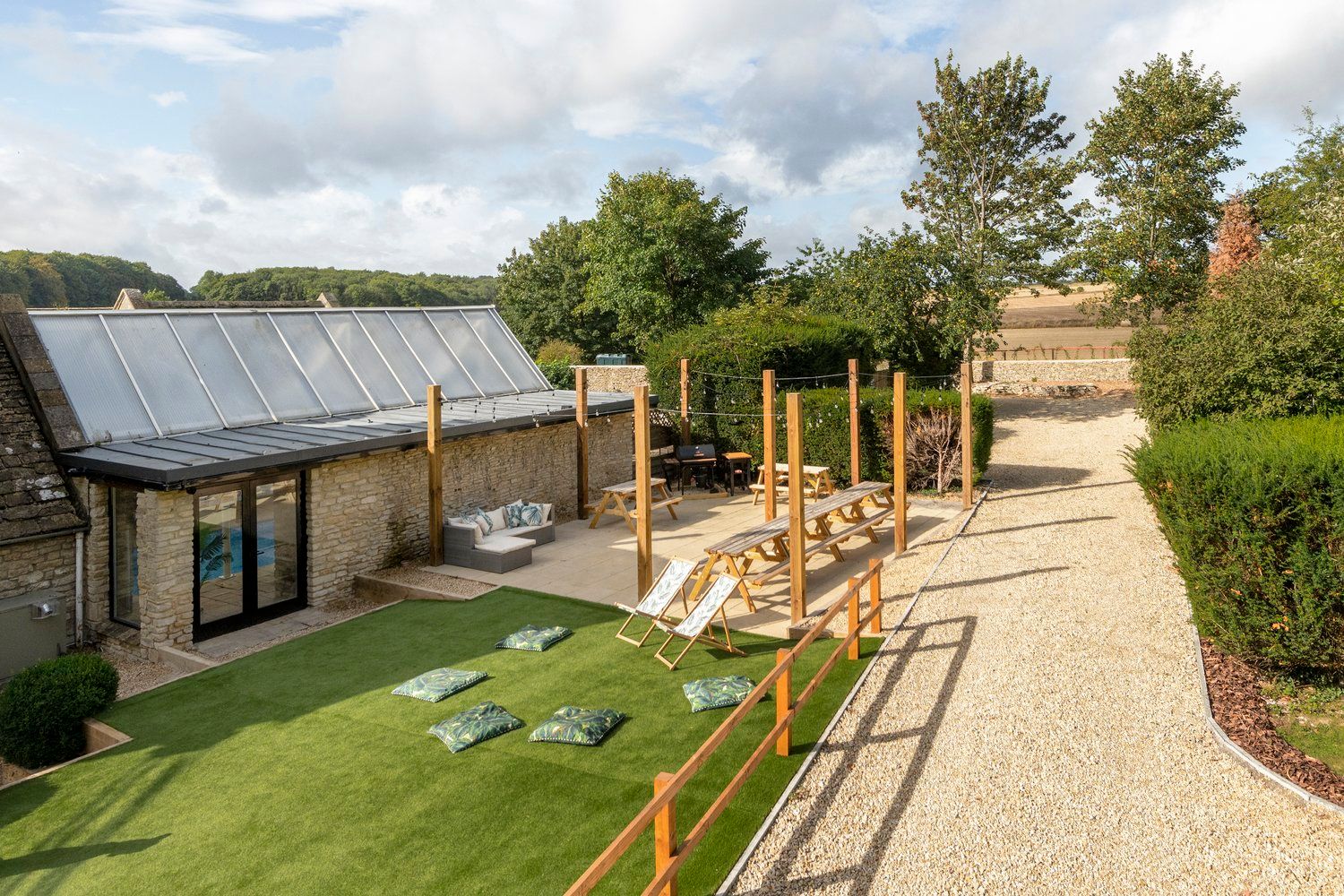 Beau's Spa House Cotswold-stone exterior with glass-roofed pool wing, terrace, picnic tables and lawn