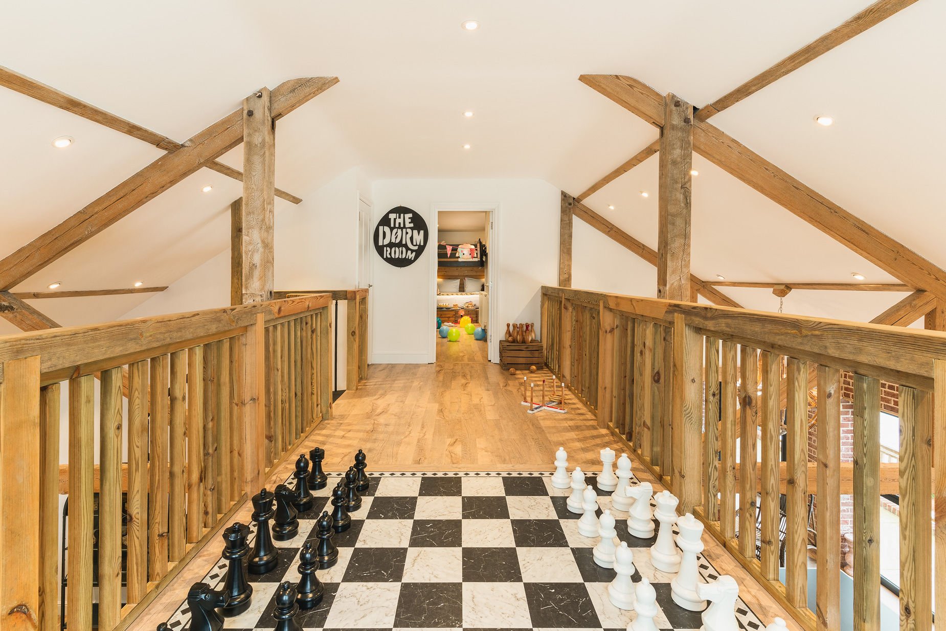 Mezzanine games loft with giant chess set, exposed beams and a 'Dorm Room' sign at the end