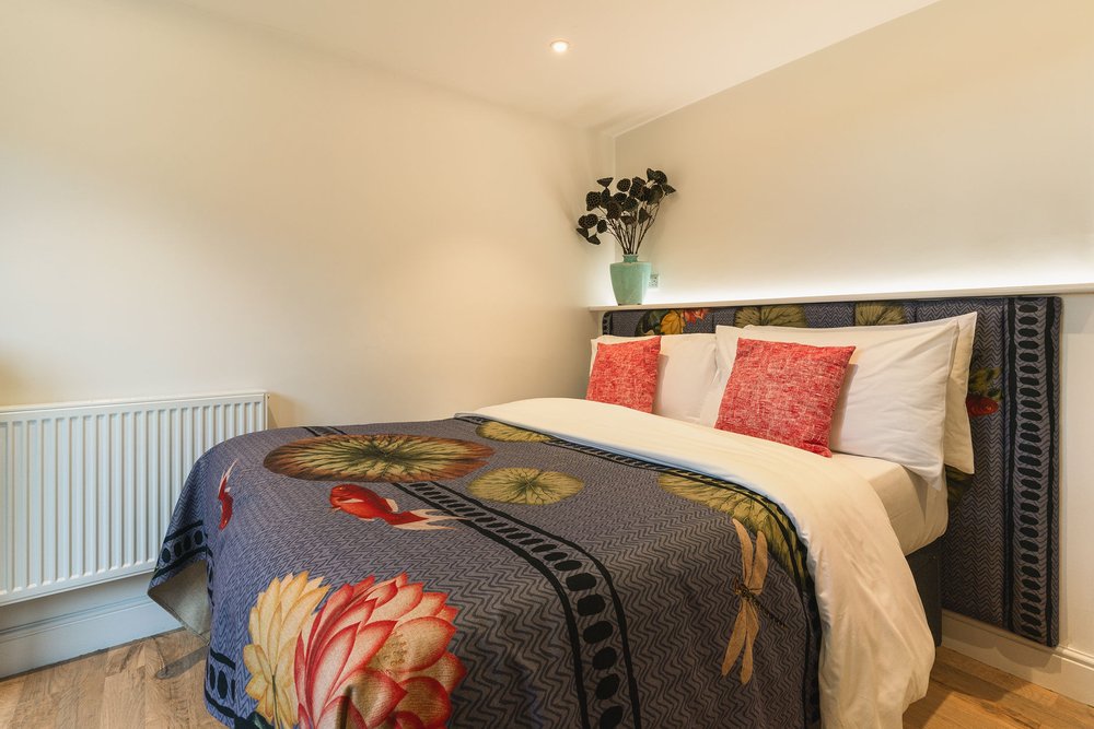 Snug double bedroom with floral lily-print bedding, coral cushions and dragonfly headboard