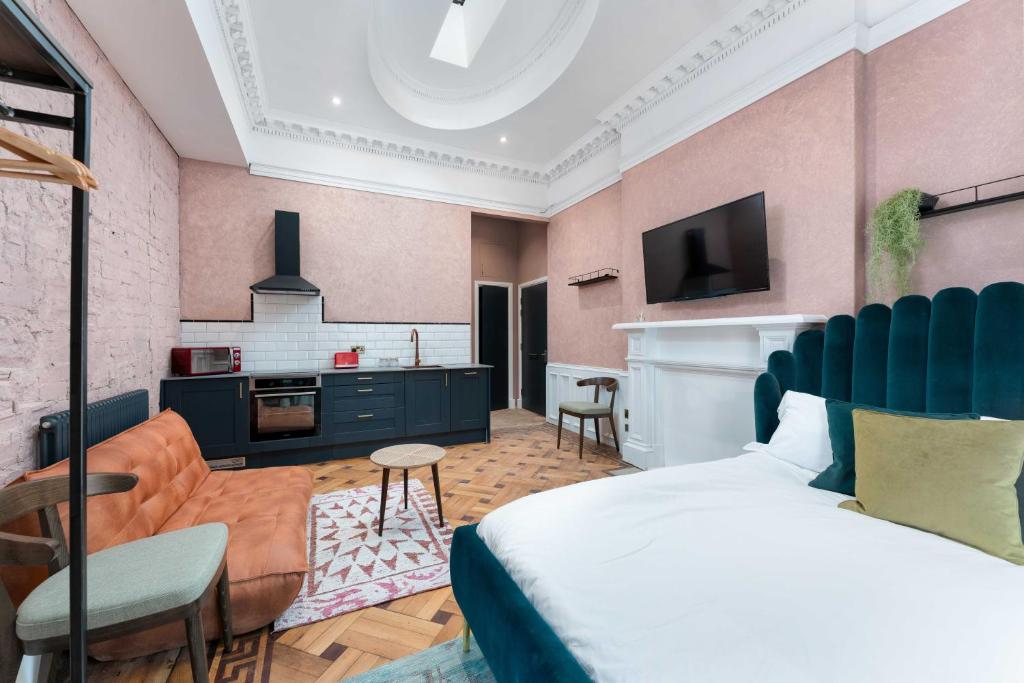 Pink-walled studio with kitchenette, green velvet bed and vintage tan sofa under a domed ceiling