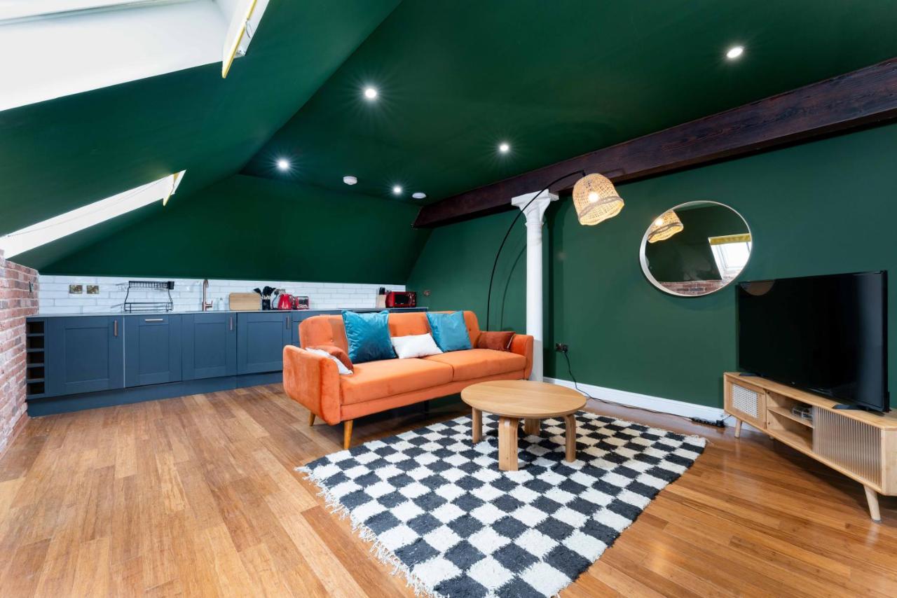 Vaulted attic flat in deep green with orange velvet sofa and chequer rug under skylights