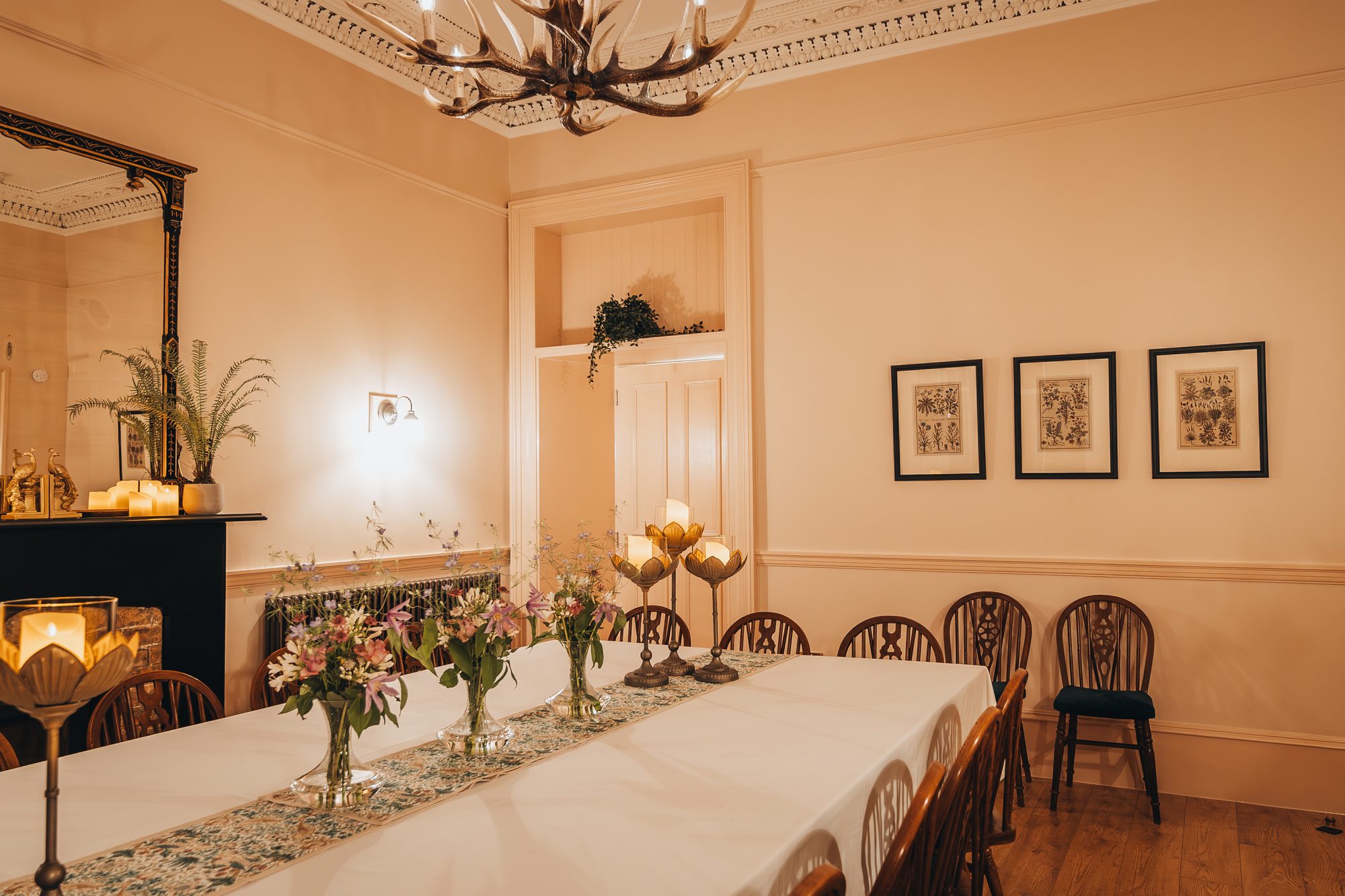 Long peach dining room at Chic Retreat set for eighteen, with antler chandelier, candlelit fireplace and rows of wheelback chairs