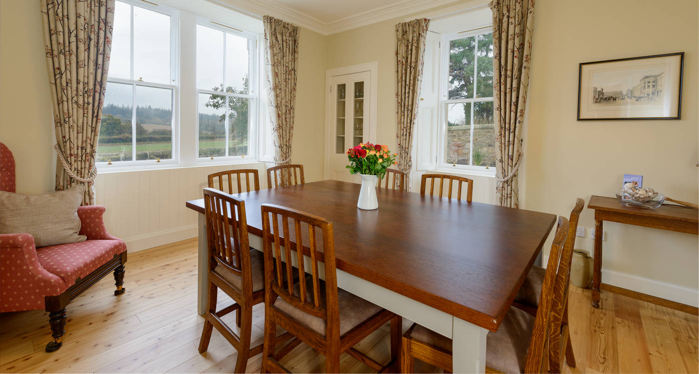 Cream dining room with mahogany table for six and tall sash windows looking onto fields