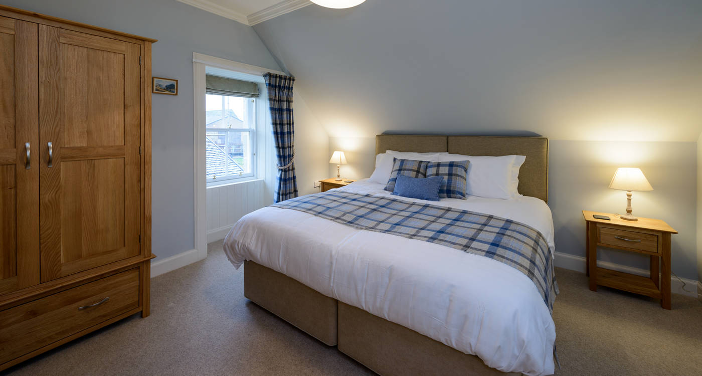 Pale-blue bedroom with king bed, oak wardrobe, tartan throw and bedside lamps