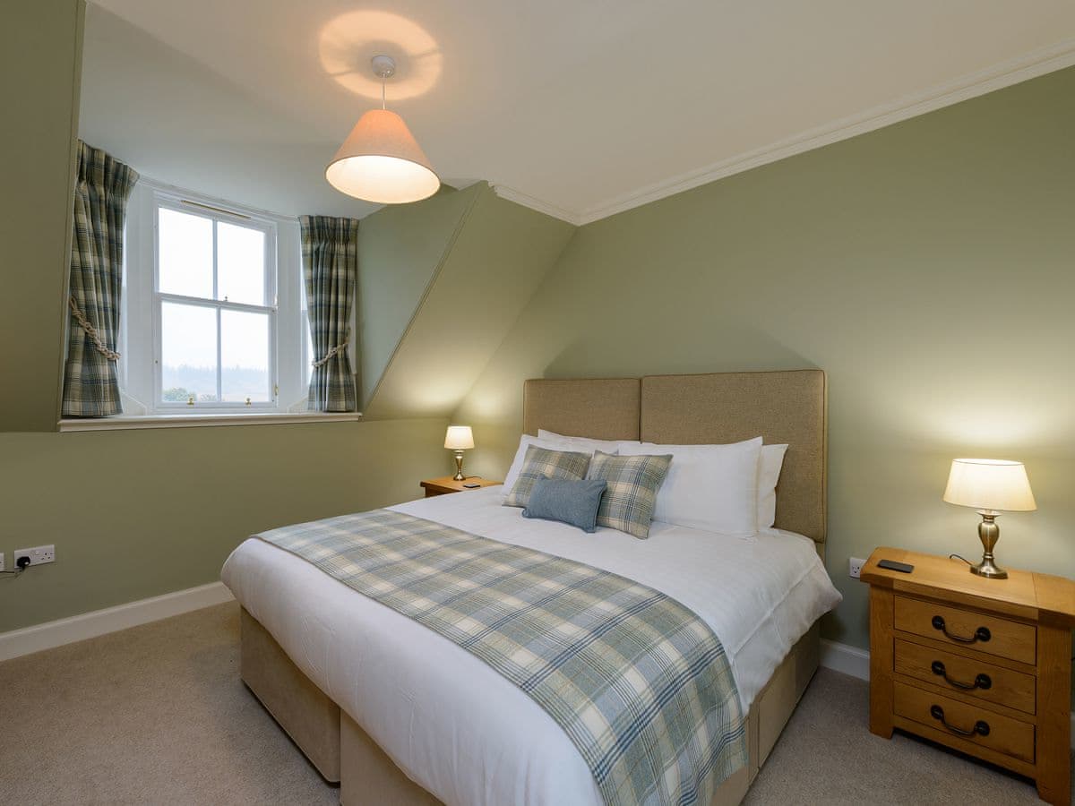 Sage green double bedroom with tartan throw, chequered curtains and brass lamps