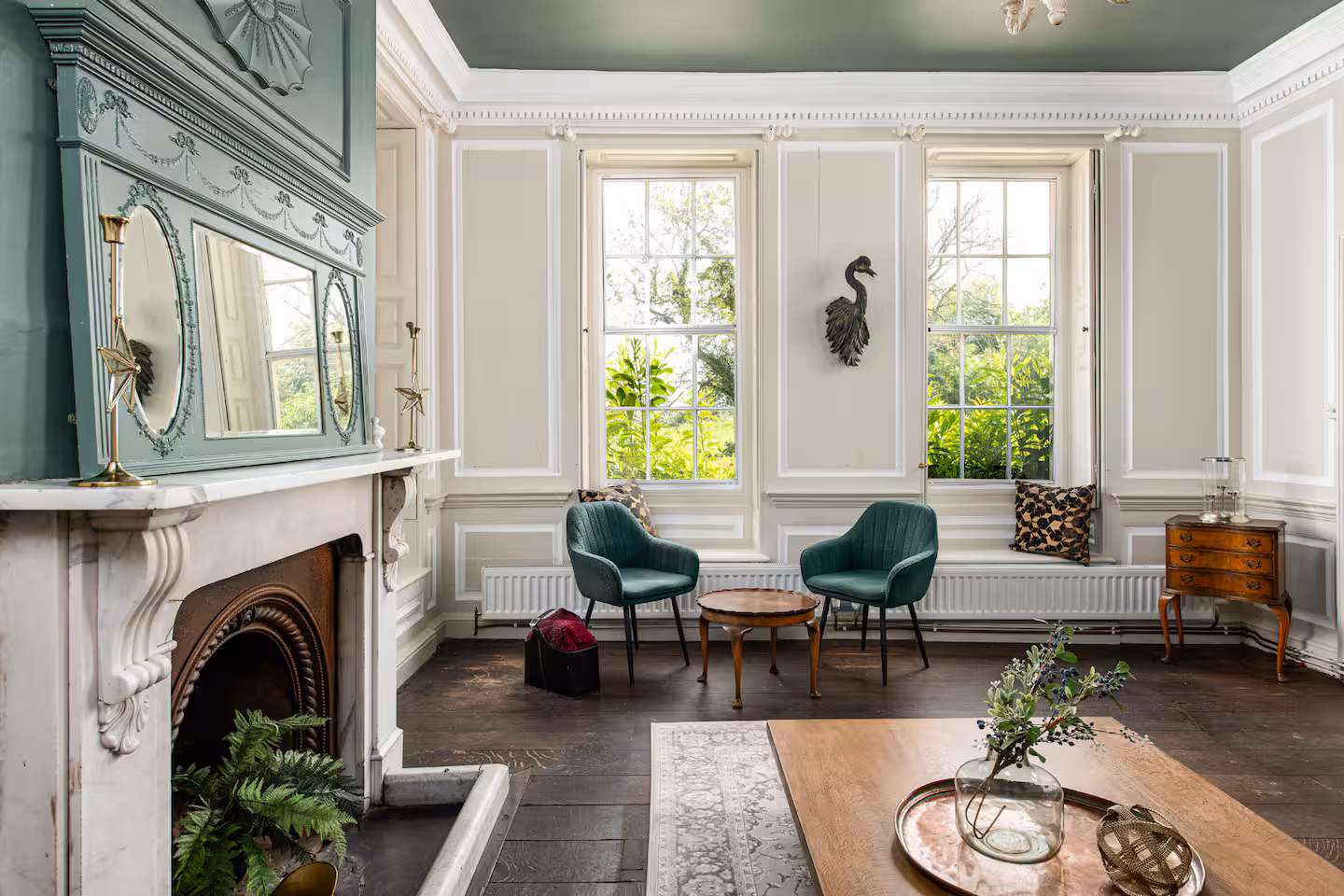 Sage green panelled drawing room with marble fireplace, two velvet armchairs and tall sash window