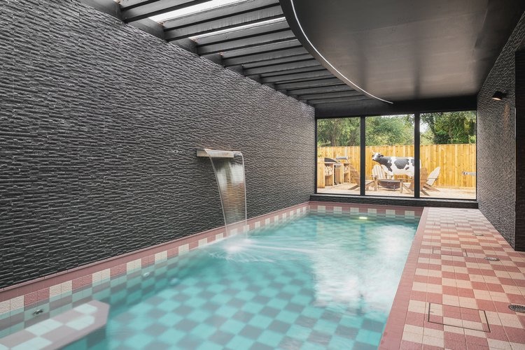 Indoor underground pool with pink and grey chequerboard tiles, dark textured stone walls and a stainless waterfall feature