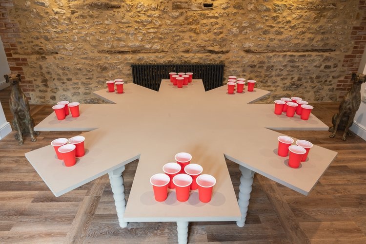 Star-shaped beer-pong table loaded with red plastic cups, flanked by stone greyhound statues against an exposed-stone wall