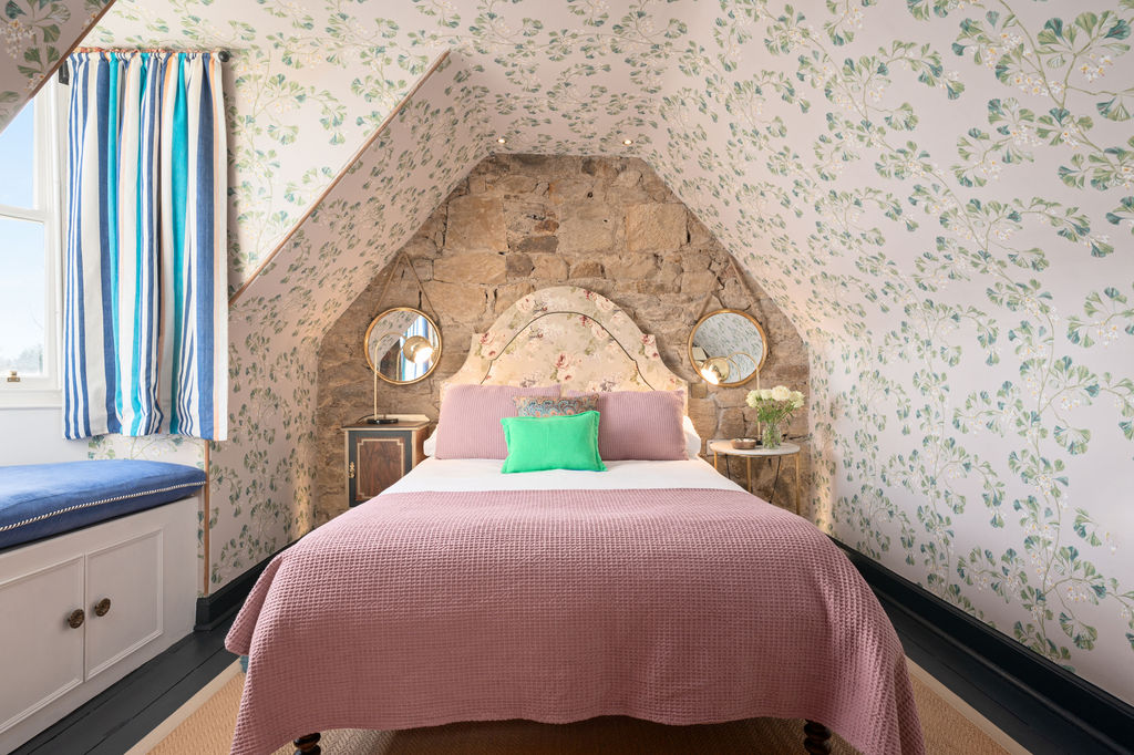 Attic bedroom with leaf wallpaper, dusty pink bedding and exposed stone arch behind the headboard