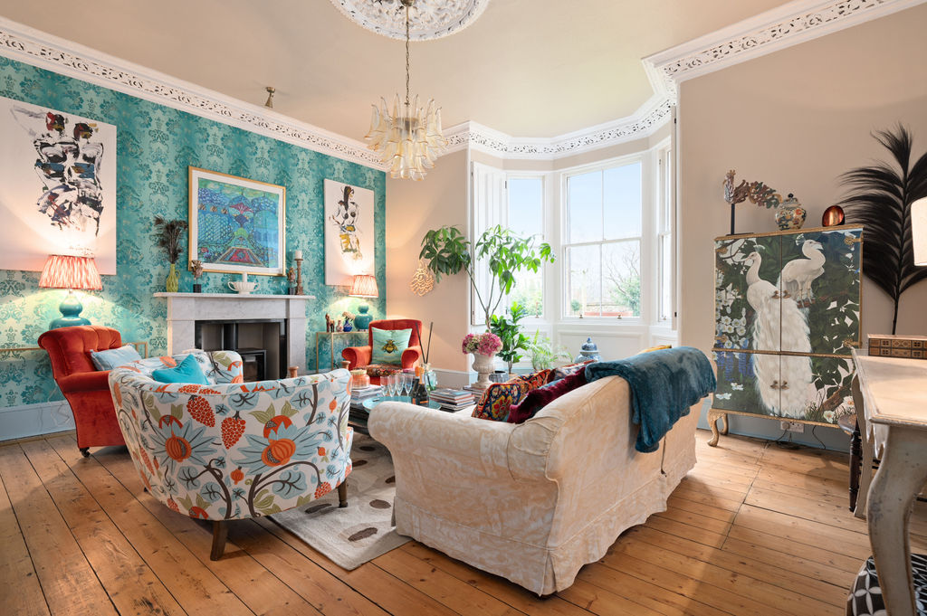 High-ceilinged Georgian sitting room with teal floral wallpaper, bay window and peacock cabinet