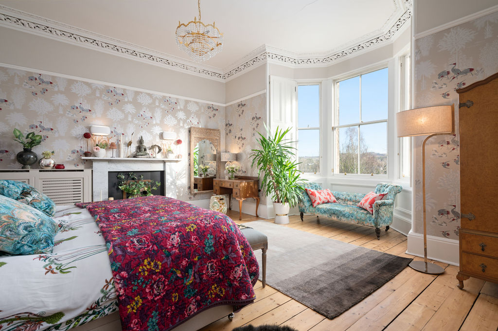 Master bedroom with crane wallpaper, fireplace, floral throw and bay window over rooftops