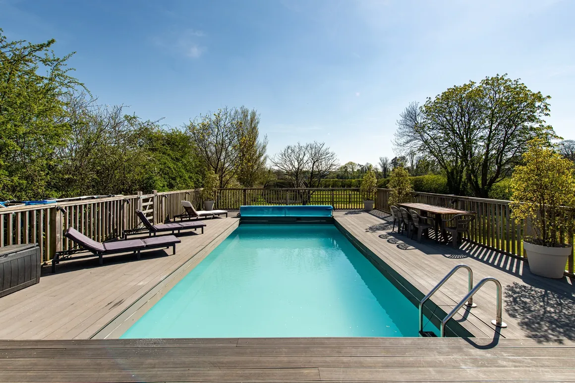 The Flowering Farm's huge private heated outdoor pool with timber decking, sun loungers and a dining table alongside