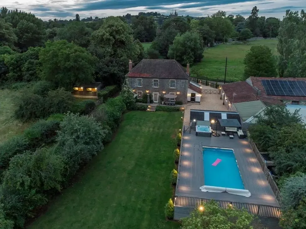 Aerial drone view of The Flowering Farm at dusk with the pool deck lit and the farmhouse windows glowing