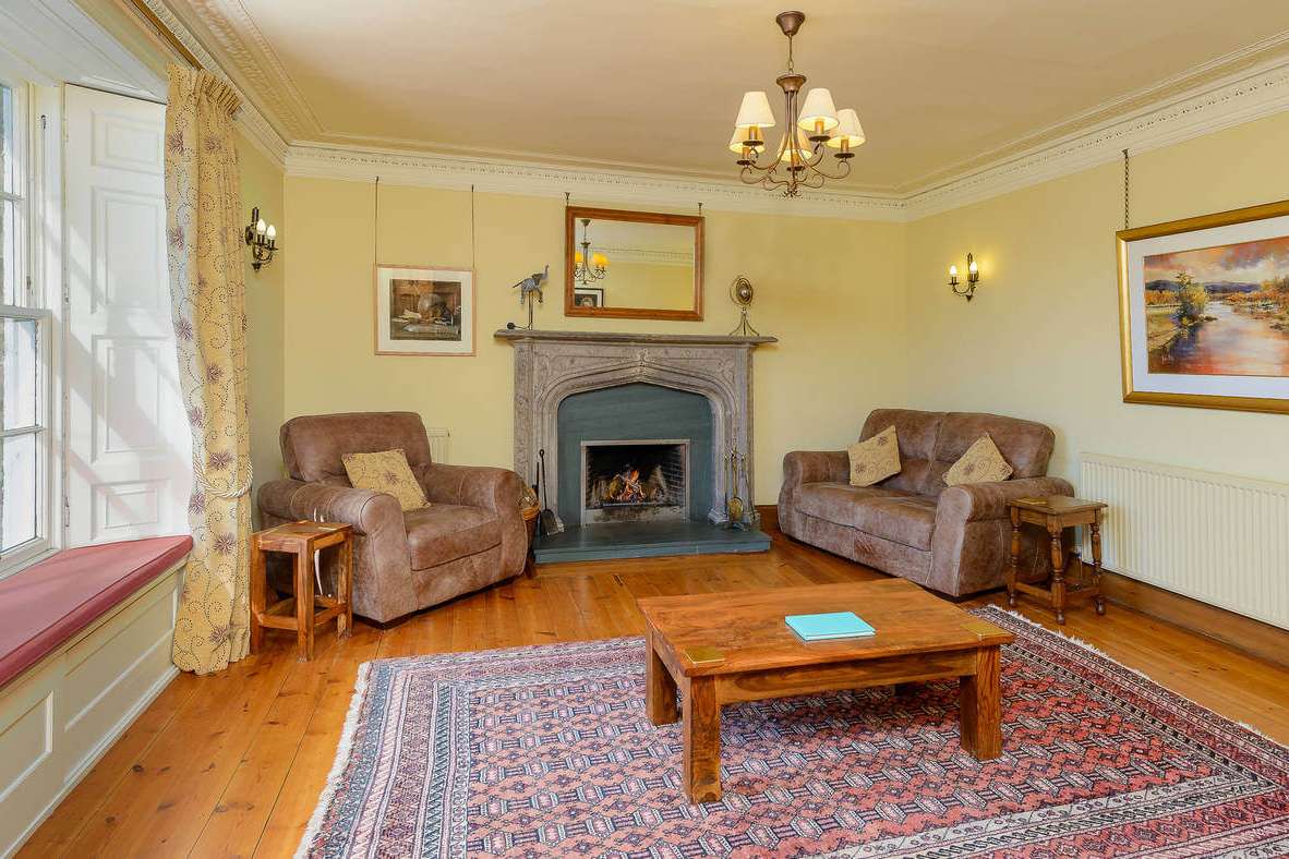 Yellow drawing room with carved stone fireplace, leather sofas and Persian rug on pine floor