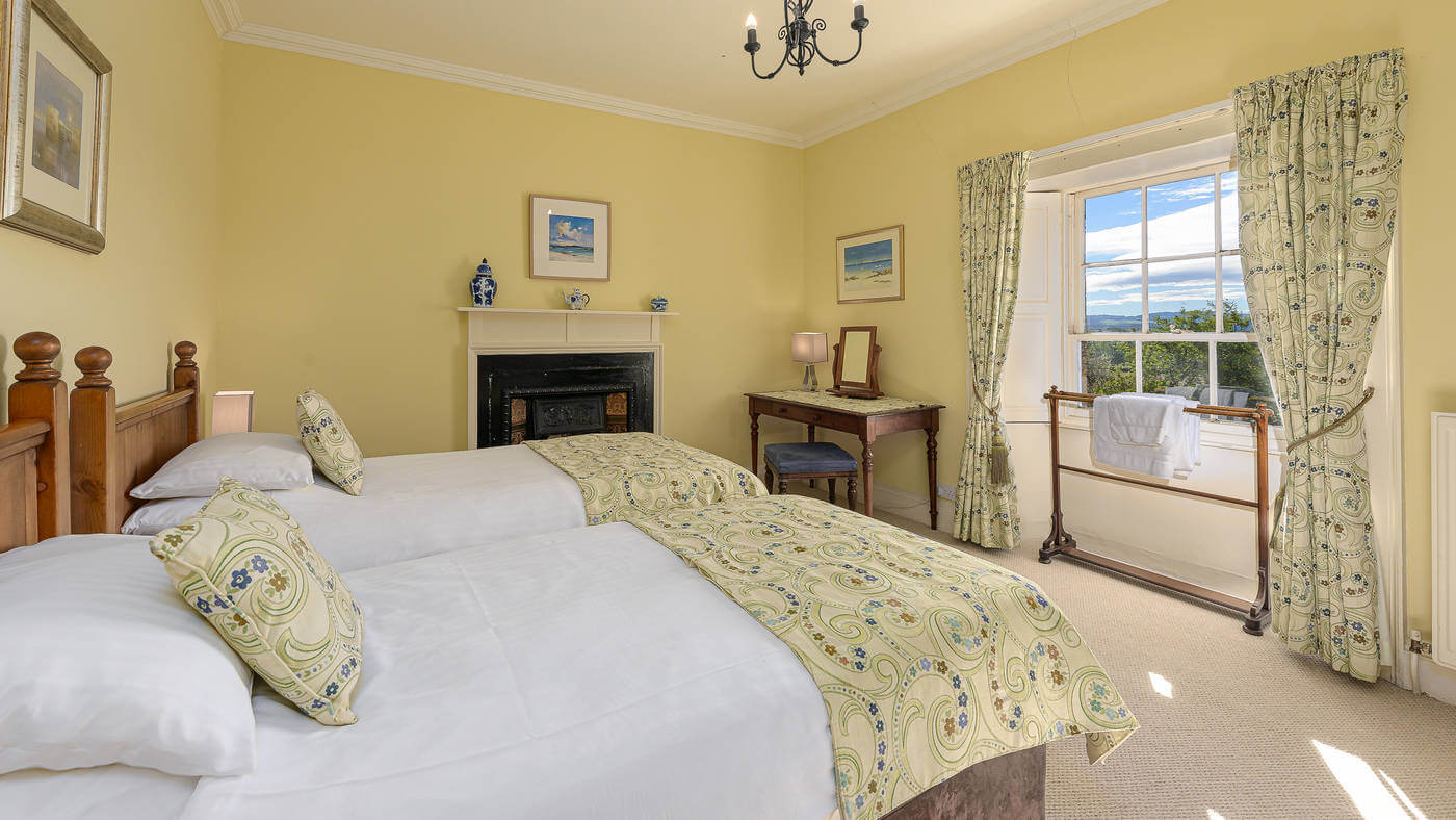 Yellow twin bedroom with cast-iron fireplace, sash window and views over the surrounding hills