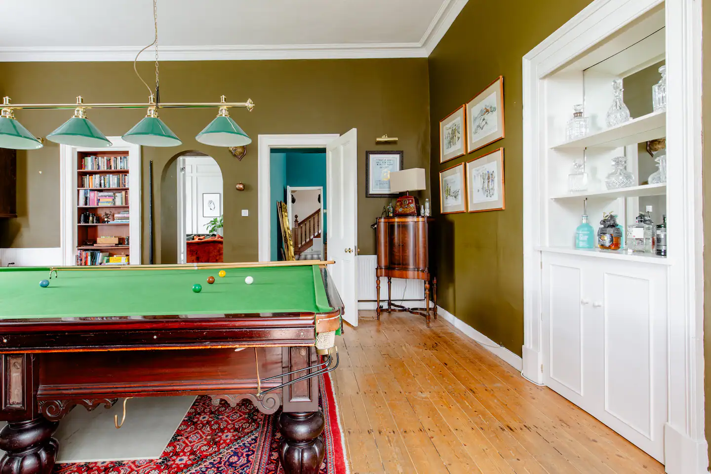 Billiards room with full-size table under green pendant lights and bookshelf beyond