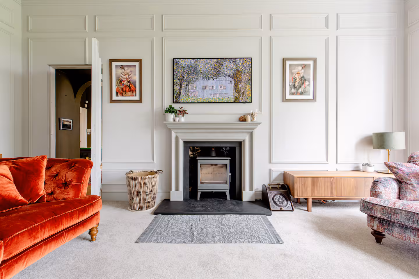 Panelled drawing room with orange velvet sofa, log burner and patterned armchair