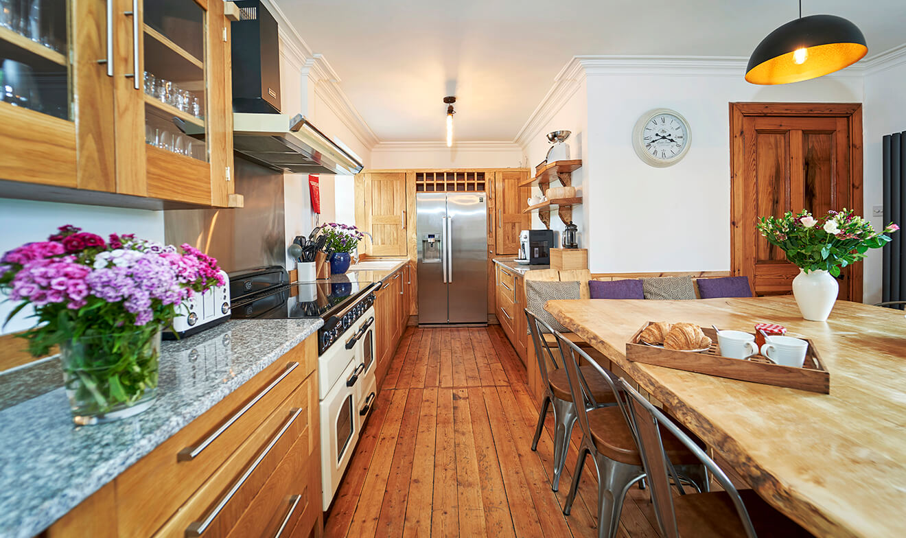 Galley kitchen with timber cabinets, granite counters, range cooker and plenty of fresh flowers