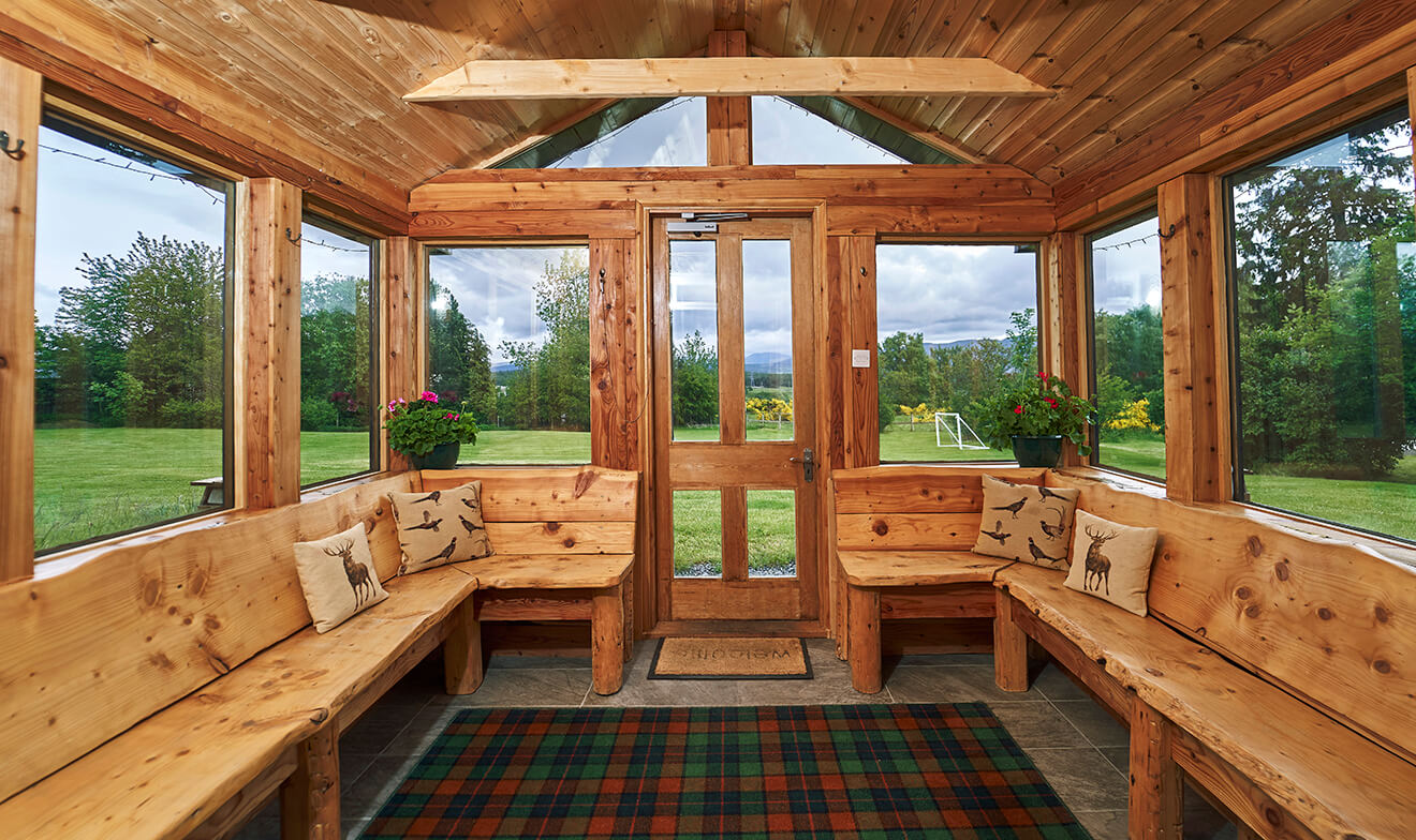 Cedar garden room with bench seating, deer-print cushions and tartan rug looking onto the lawn