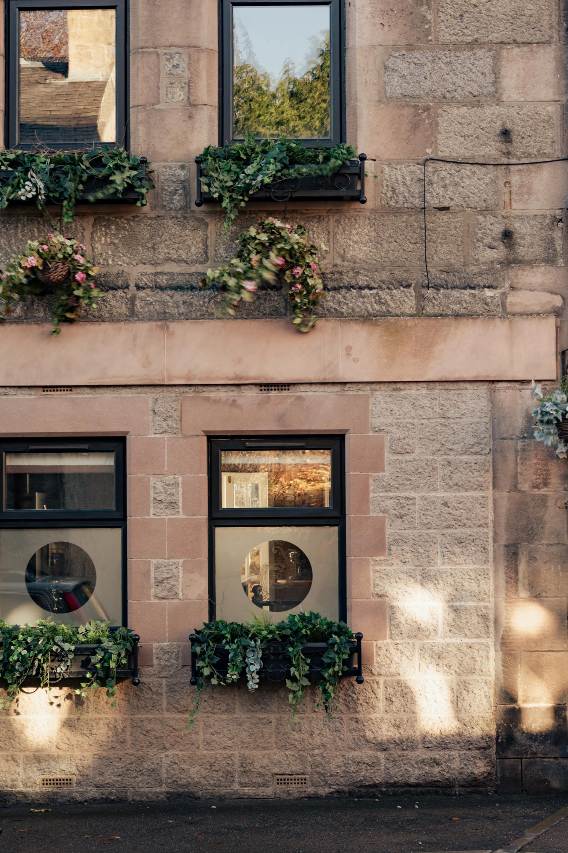 Pink sandstone townhouse facade with planted window boxes, sash windows and original stone detailing on a Cairngorms village street