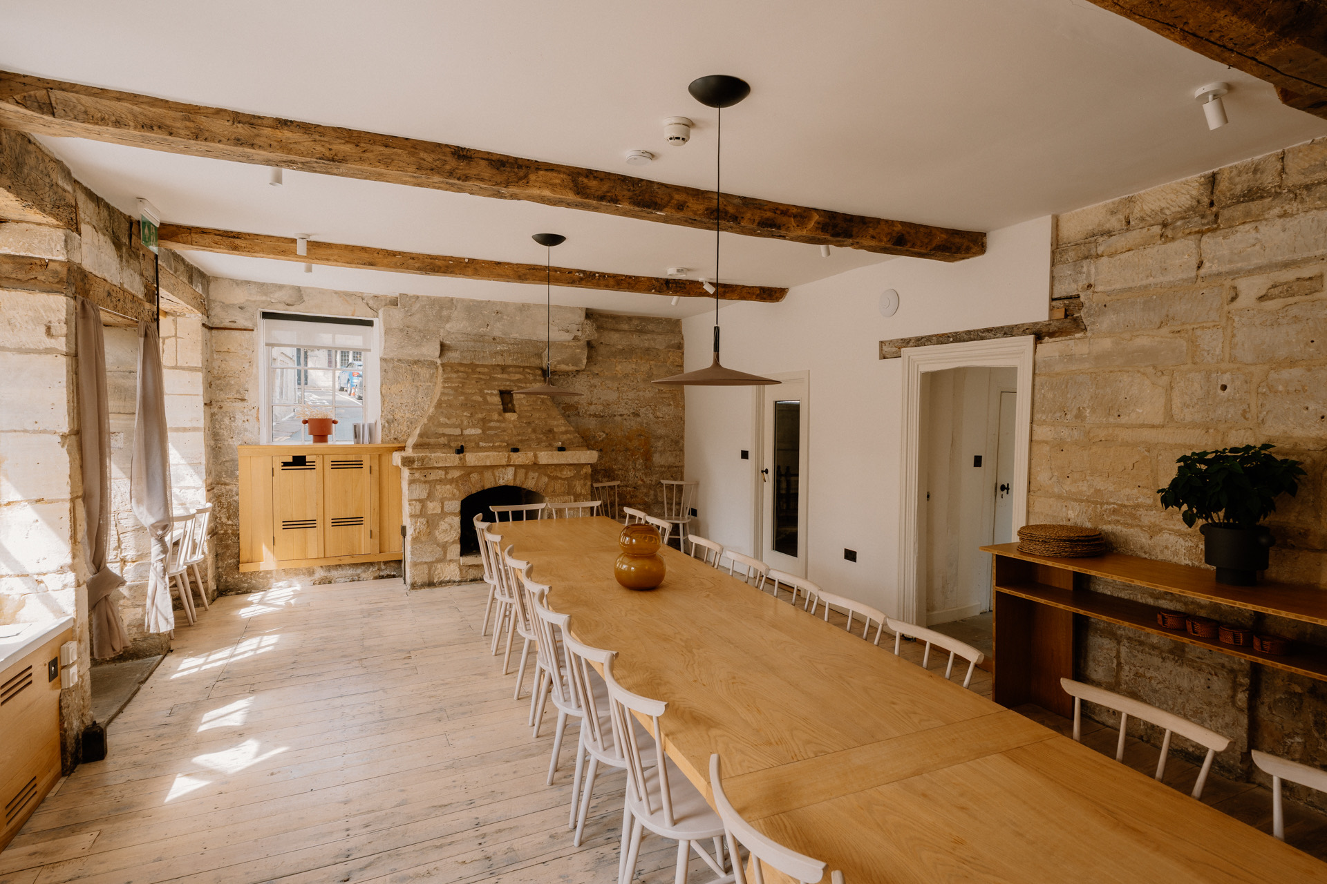 Long timber dining table lined with white spindle chairs under exposed beams in a former embroidery workshop