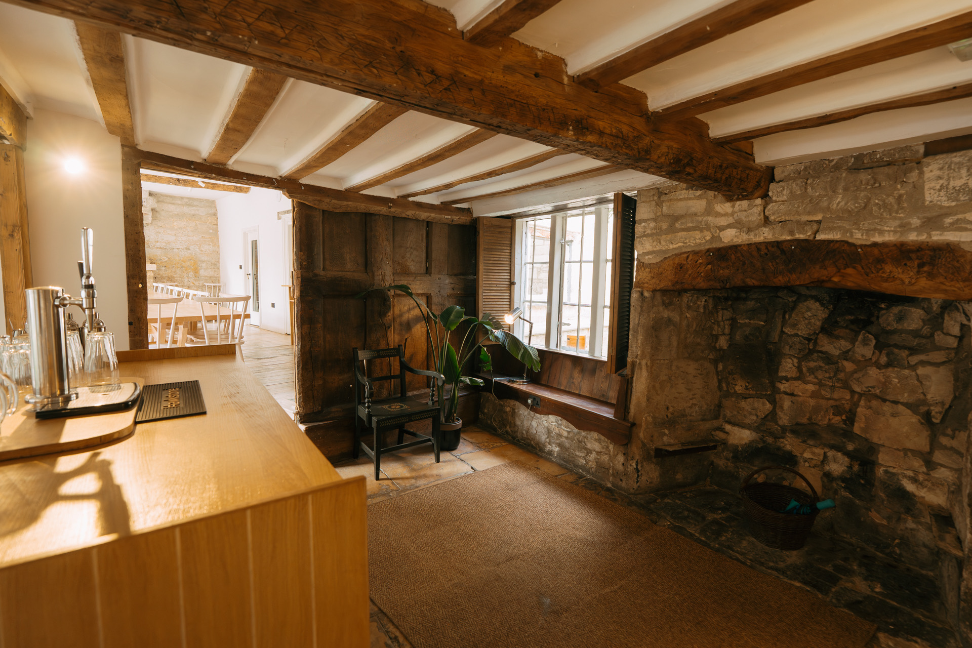 Bar counter with beer taps beside a huge stone inglenook under a beamed ceiling
