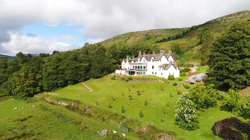 Aerial view of the white mansion in a Highland glen with sheep grazing in the foreground