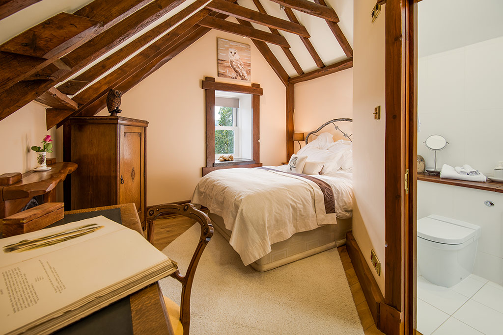 Eaves bedroom with exposed beams, wrought-iron bedstead and antique wardrobe under the rafters