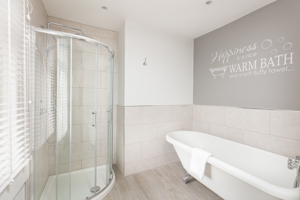 Bathroom with white clawfoot tub, corner shower and Warm Bath wall decal in soft grey