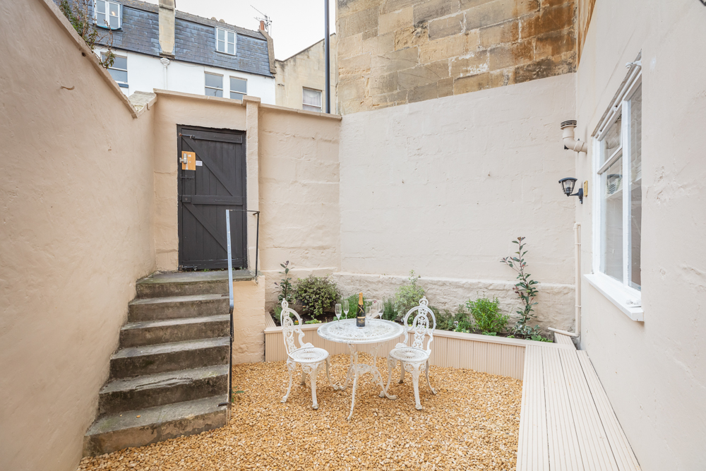 Cream-walled rear courtyard with gravel floor and white bistro set holding chilled prosecco