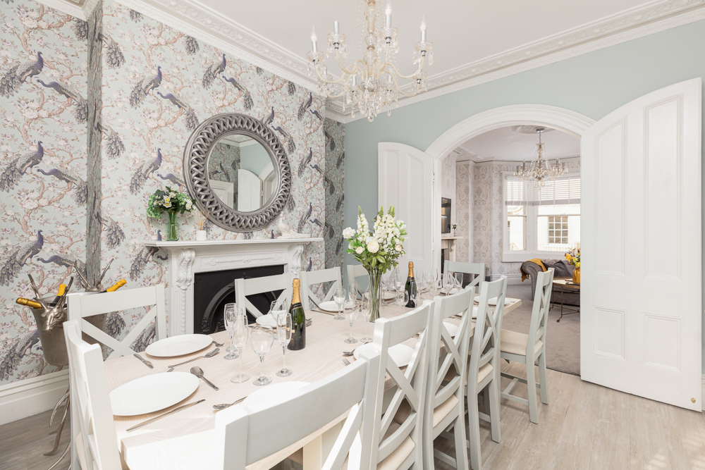 Peacock-wallpapered dining room with crystal chandelier, set table and arched doorway through to lounge