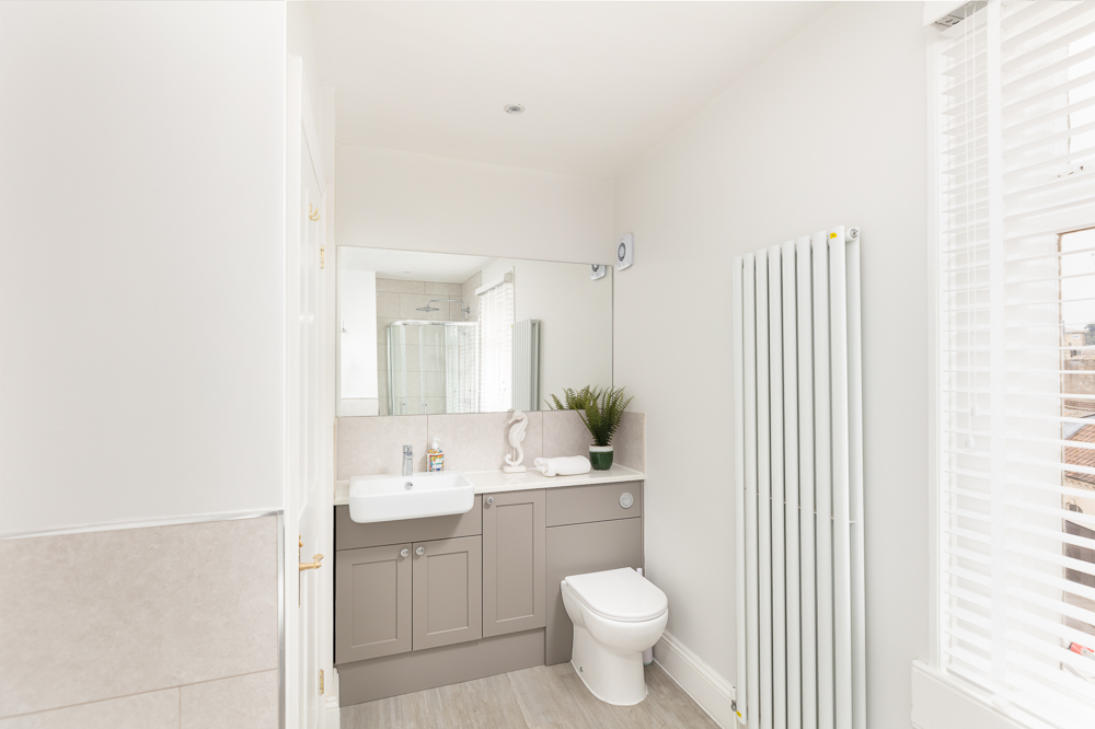 Modern bathroom with grey vanity, large mirror and tall vertical radiator beside sash window