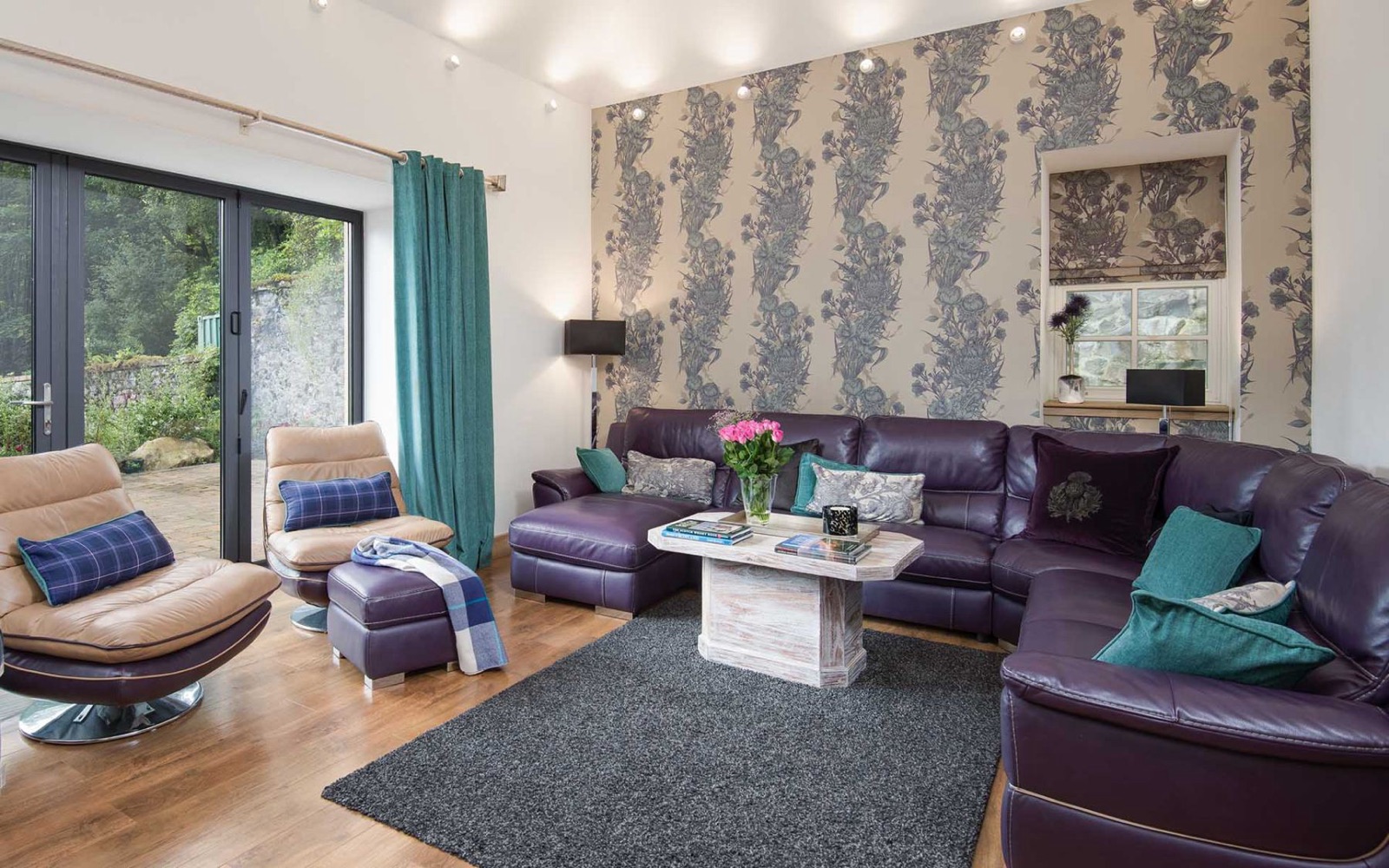 Lounge with purple leather corner sofa, teal cushions and bi-fold doors to the garden