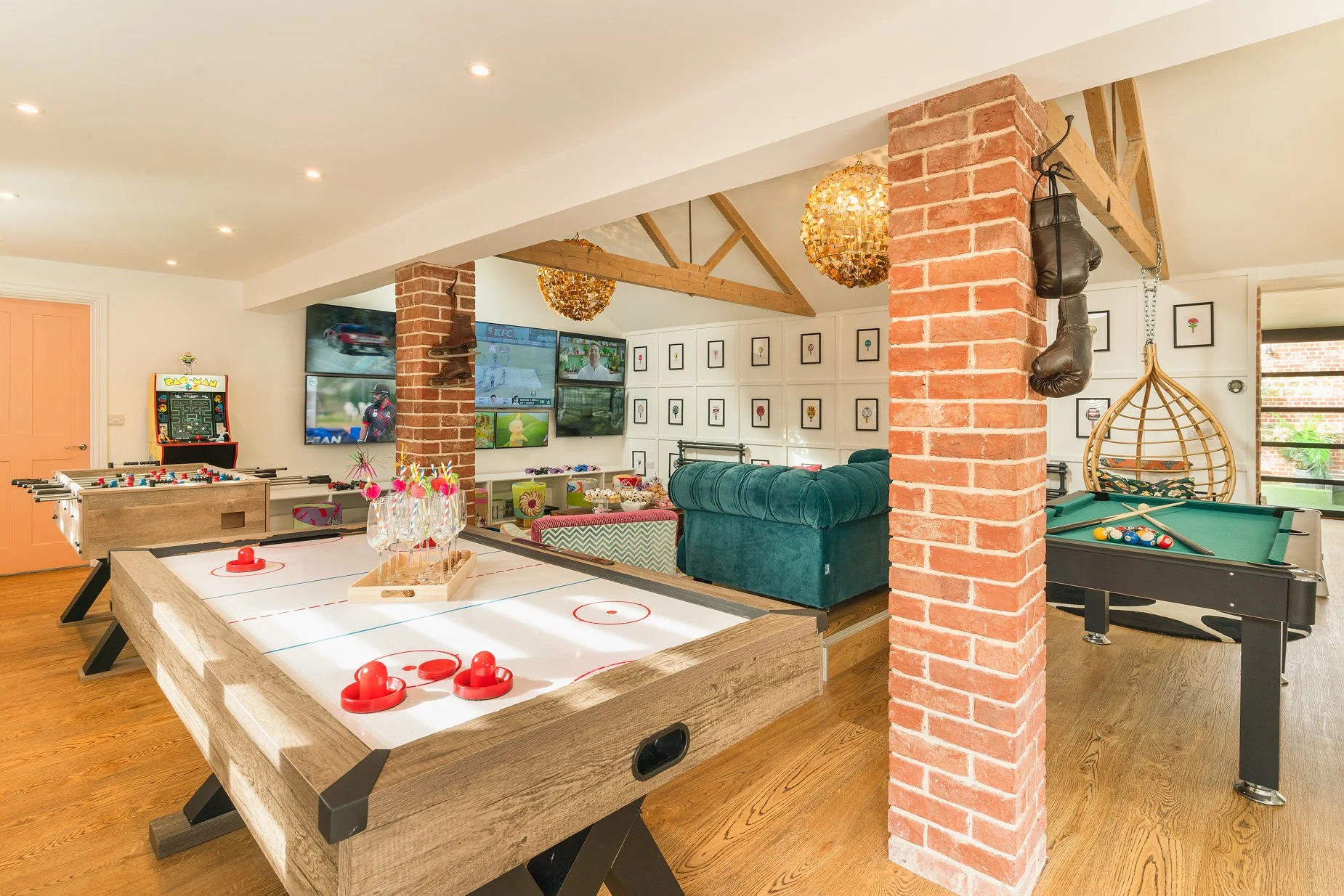 Pinkertons games room with air-hockey table, foosball, arcade cabinet, wall of TVs, green chesterfield, hanging rattan chair and pool table under exposed-brick columns