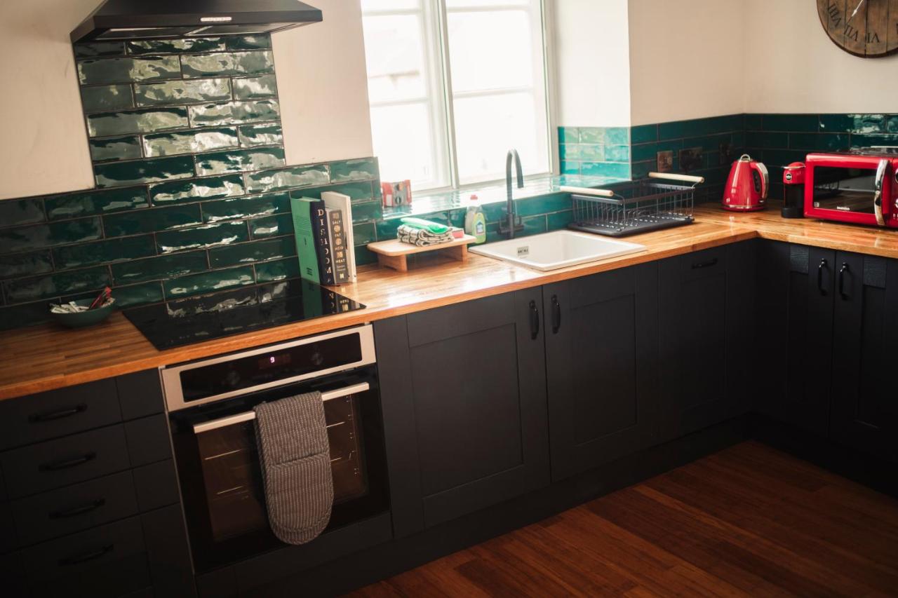 Black shaker kitchen with butcher-block worktop, green gloss metro tiles and red kettle and toaster
