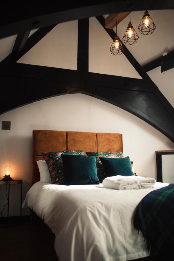Loft bedroom under exposed black A-frame trusses with tan suede headboard and geometric pendant lights