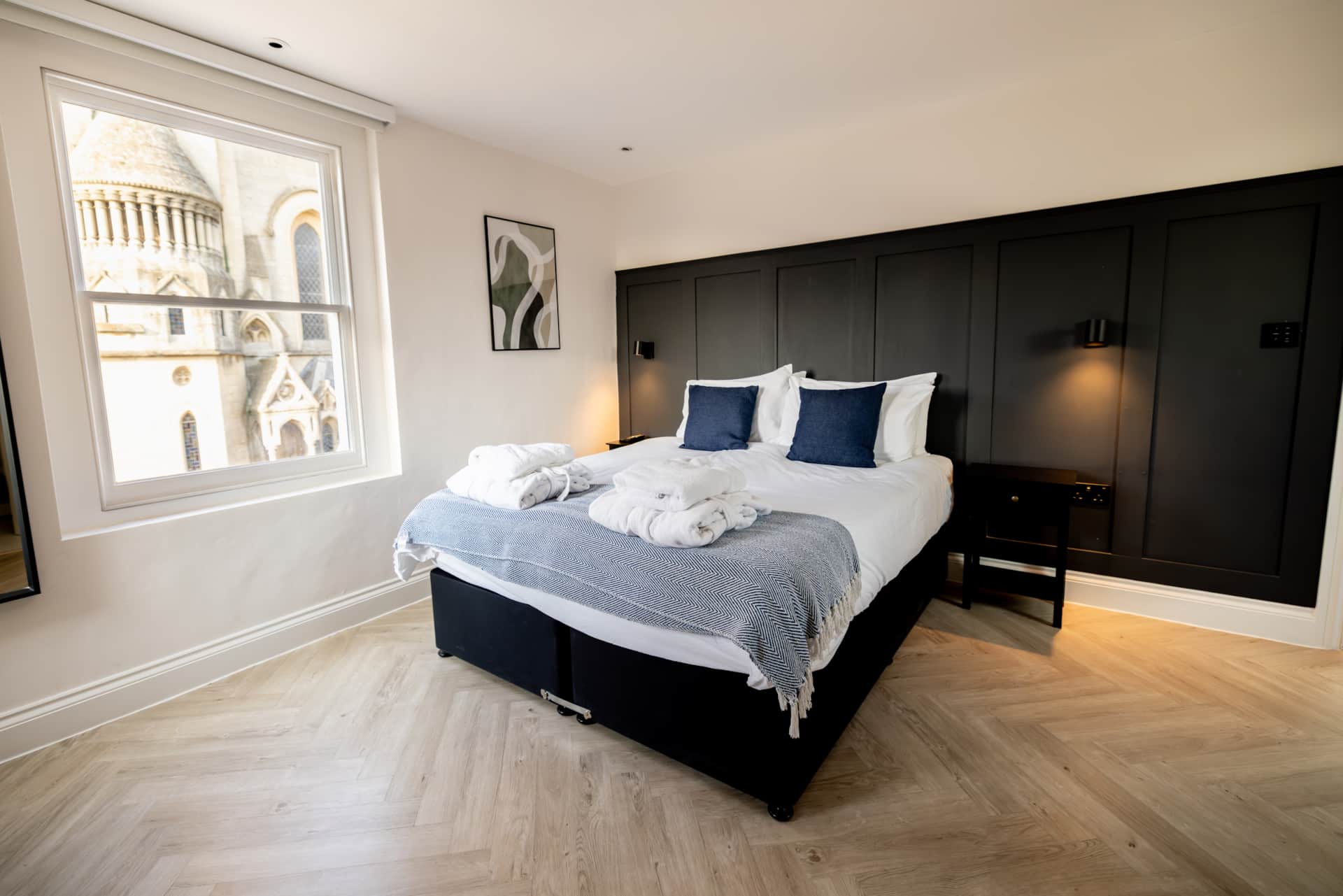 Bedroom with black panelled feature wall, herringbone floor and a sash window framing Bath Abbey