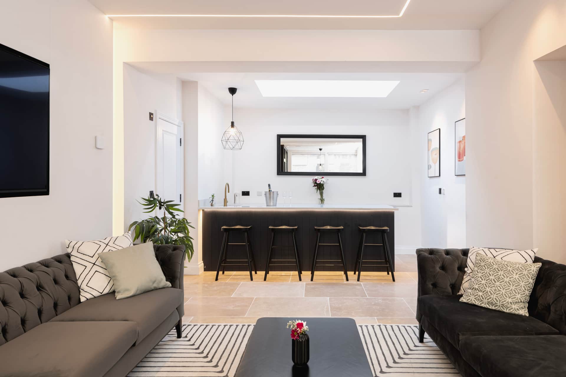 Open lounge with twin grey velvet Chesterfields and a black bar with four stools through the back arch