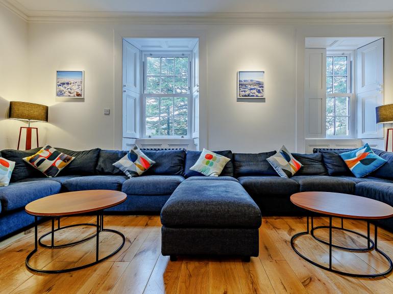 Large blue corner sofa in the lounge with two round coffee tables and tall sash windows, The Scottish Lodge