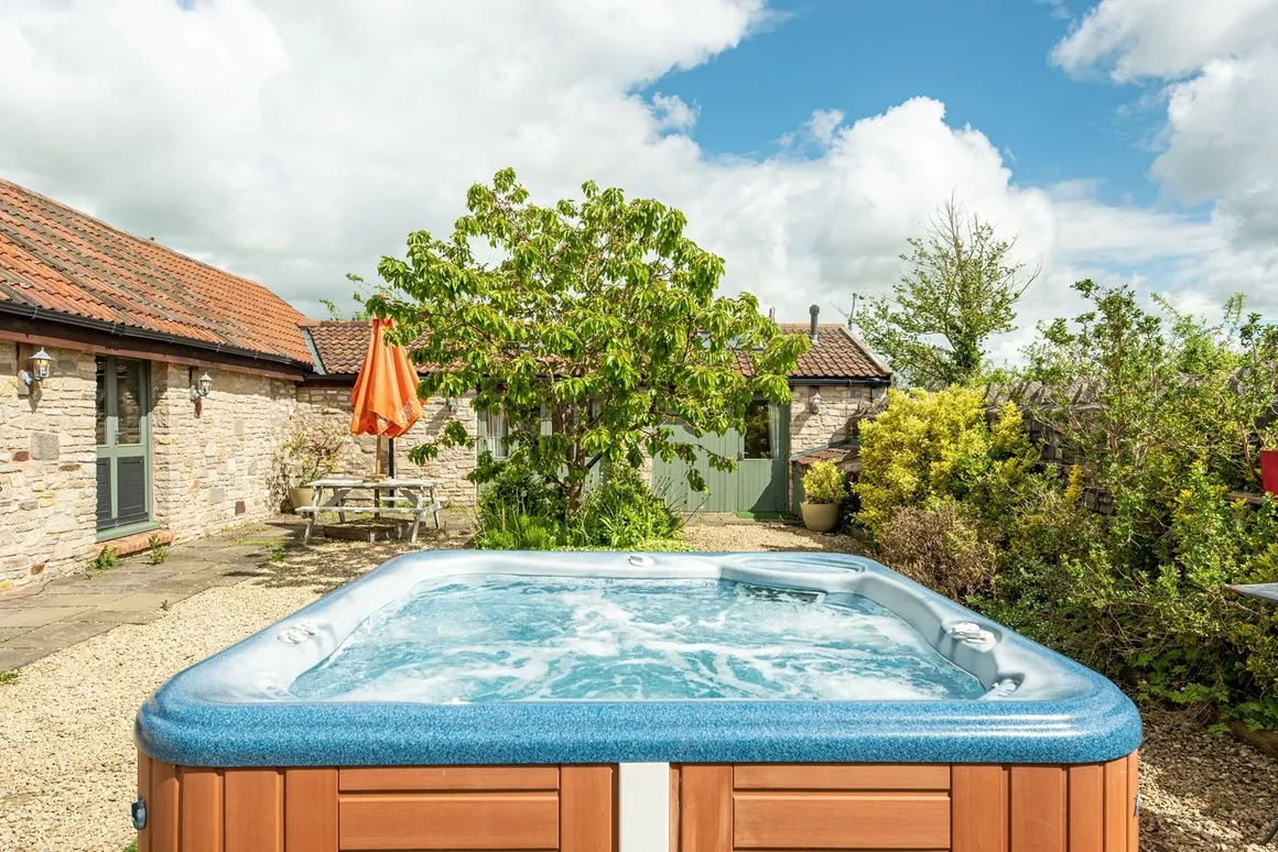 Outdoor hot tub on a courtyard patio with stone barn outbuilding and orange tree behind